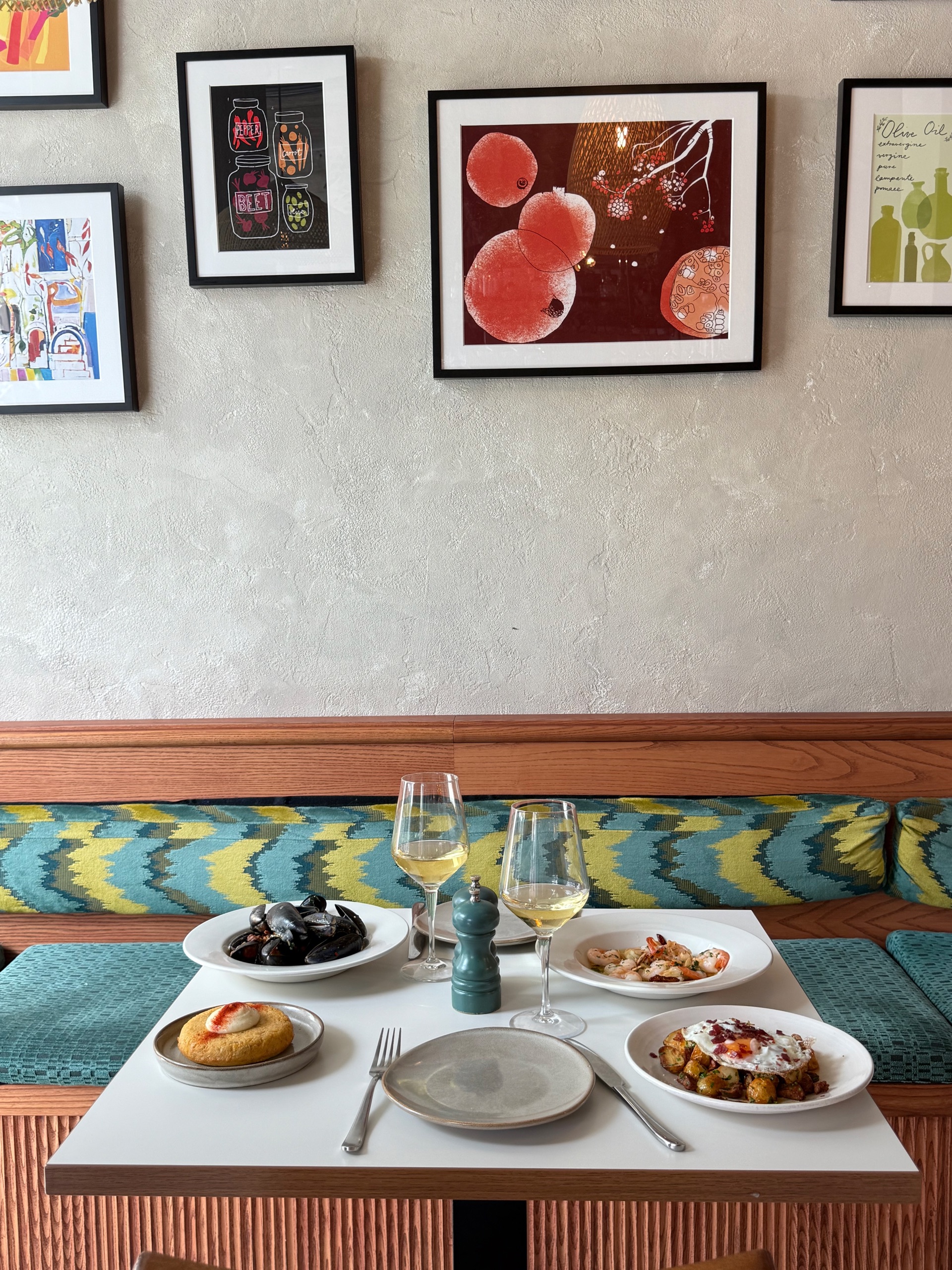 A banquette table set with mussels, prawns and tortilla beneath La Gamba's colourful art wall, two glasses of white wine
