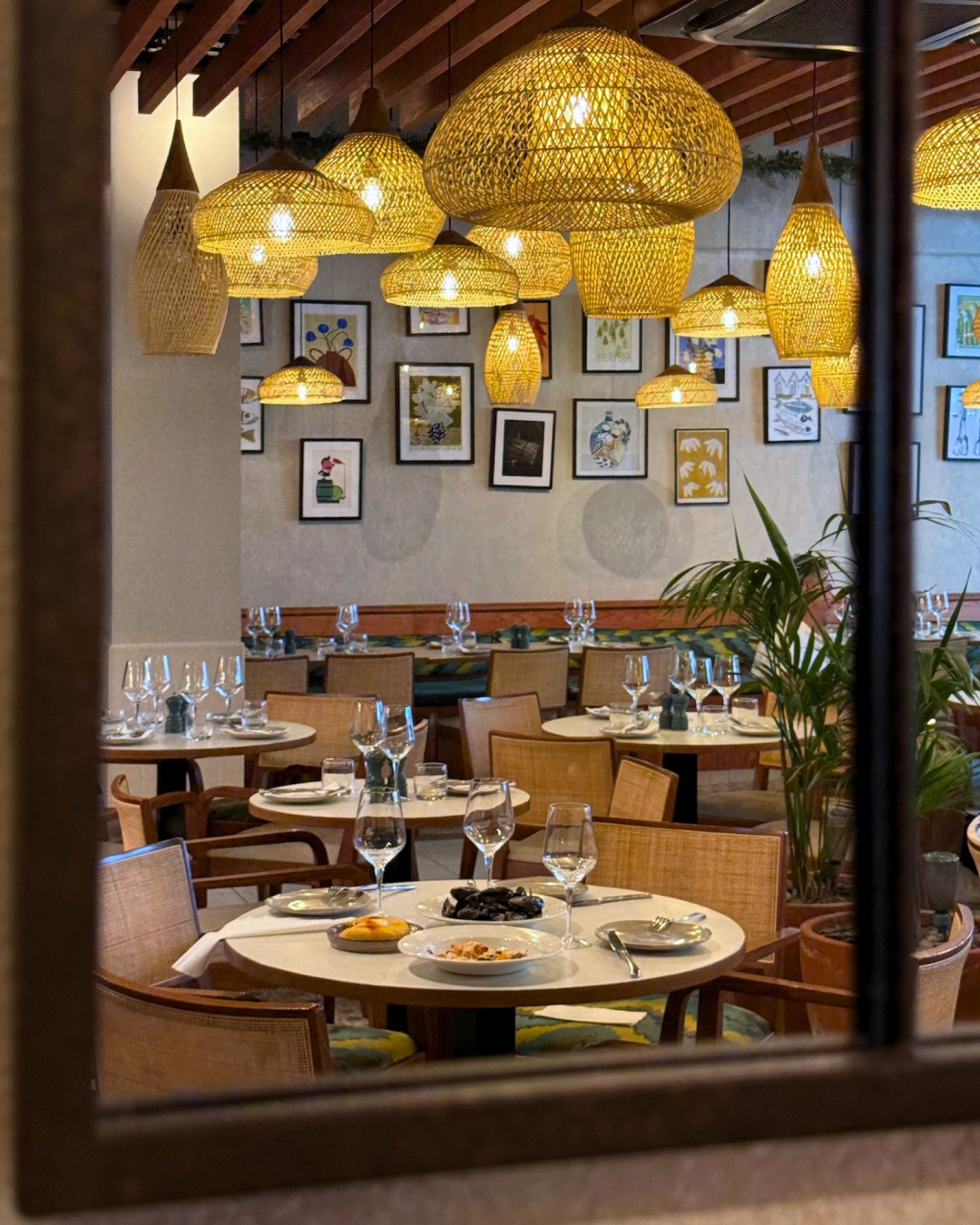 La Gamba's dining room seen through the mirror, with rattan lamps, an art wall and tables laid for lunch